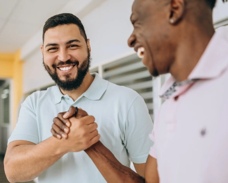 Two men smiling and shaking hands warmly indoors.